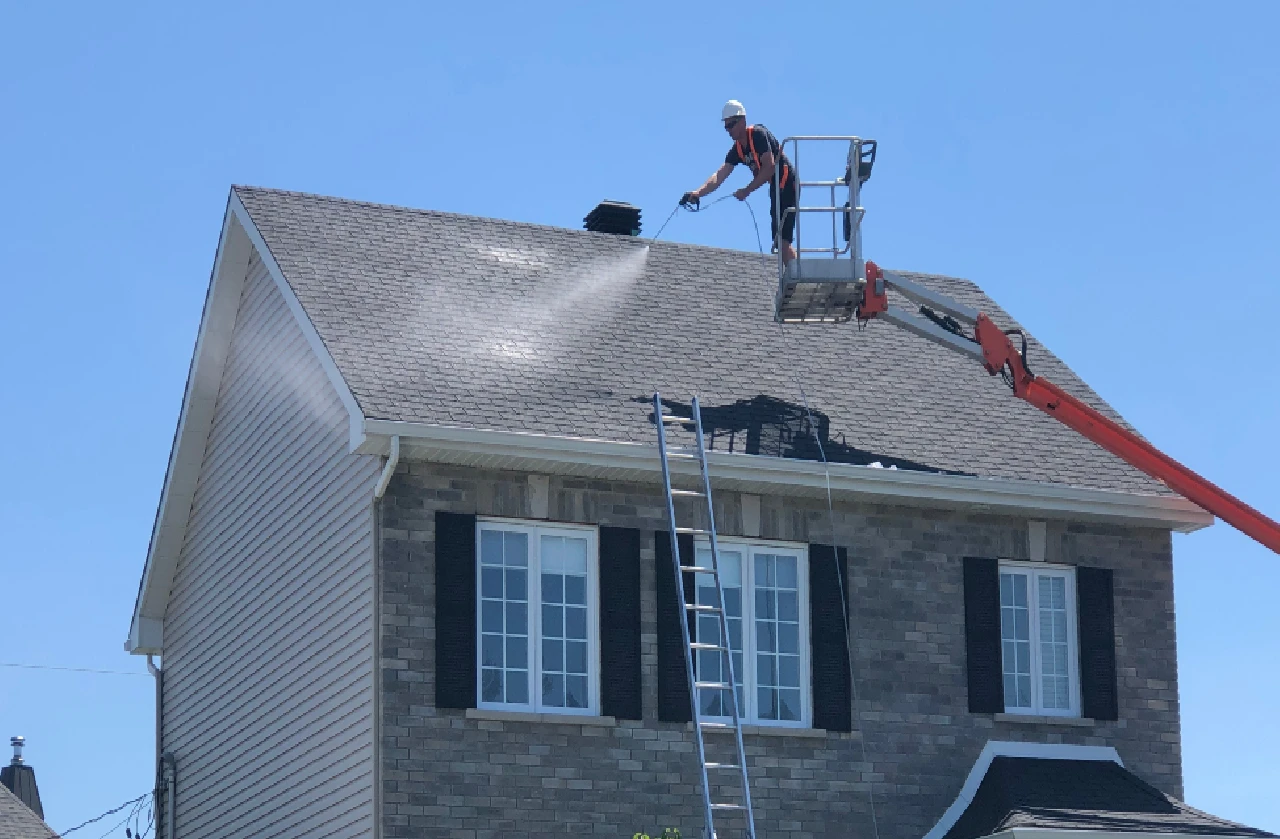 Worker applying nano coating to asphalt shingles on a residential roof using a lift, enhancing durability and lifespan against extreme weather conditions.